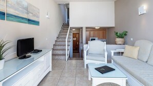A modern living room with a flat-screen TV, a white sofa, a coffee table, and a staircase leading to an upper level. - Apartamentos Punta Marina by LIVVO (Pajara)