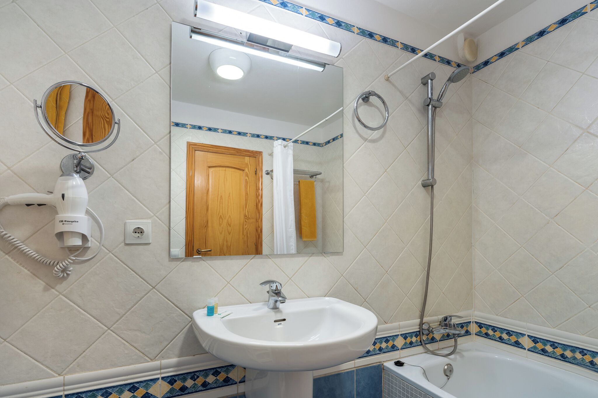 Une salle de bain équipée d’un lavabo, d’un miroir, d’un sèche-cheveux et d’une douche.