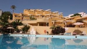 Un hotel con piscina, varios balcones y zonas de estar al aire libre.