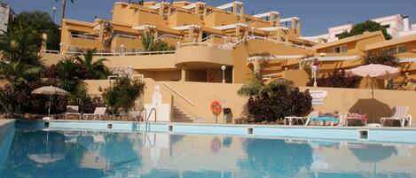 A hotel with a swimming pool, multiple balconies, and outdoor seating areas.