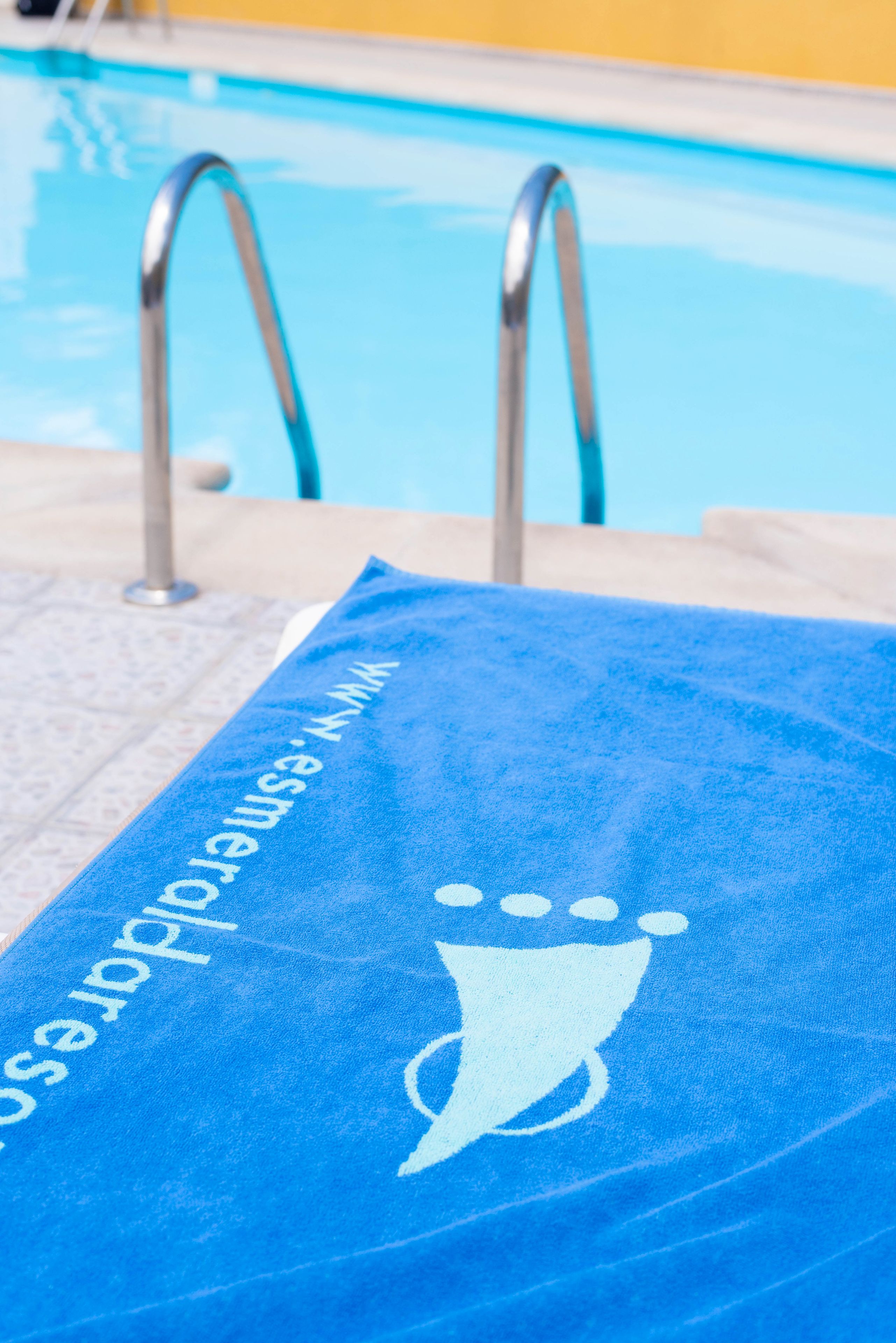 A blue towel with a white logo and text, placed on a poolside area.