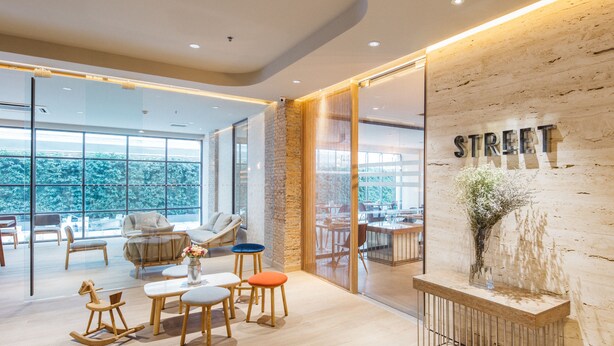 A modern interior with a wooden reception desk, a seating area with a sofa and chairs, and large windows offering a view of the outdoors. - Clef Hotel (Samut Prakan)