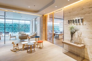 A modern interior with a wooden reception desk, a seating area with a sofa and chairs, and large windows offering a view of the outdoors. - Clef Hotel (Samut Prakan)