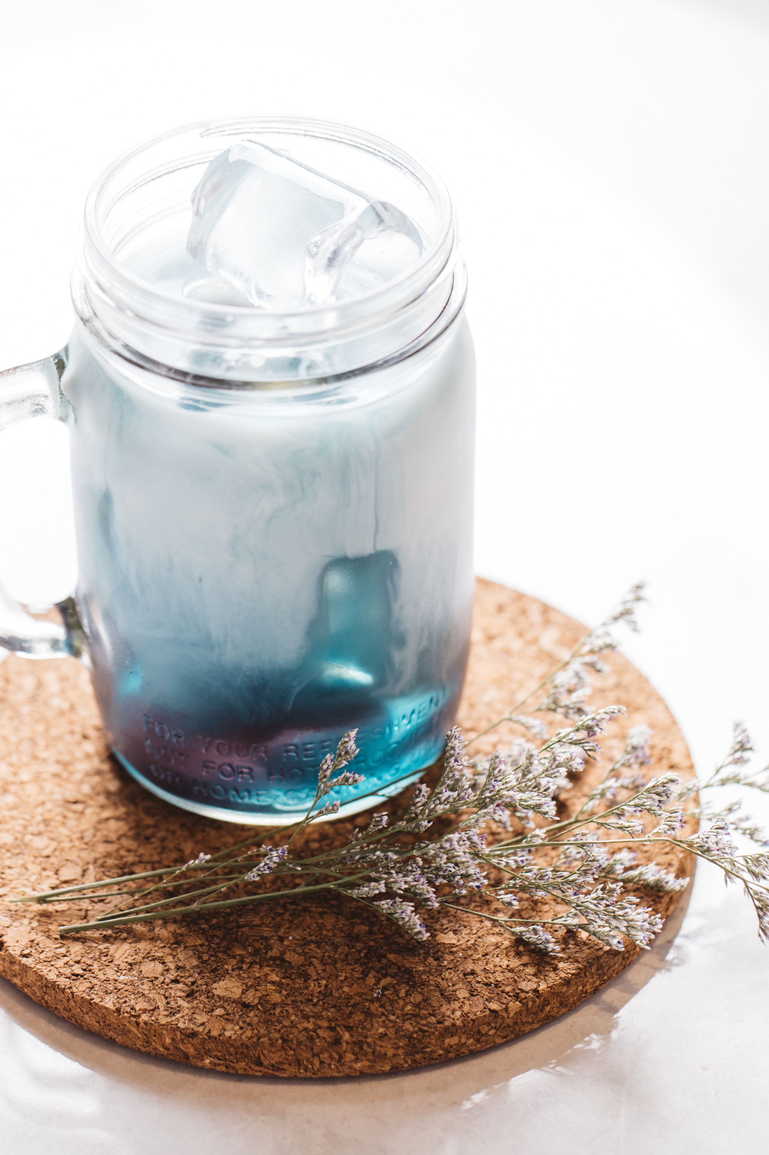 A clear glass mug with ice cubes on a cork coaster.