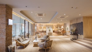A spacious lounge area with comfortable seating, a visible staircase, and a brick wall. - Clef Hotel (Samut Prakan)