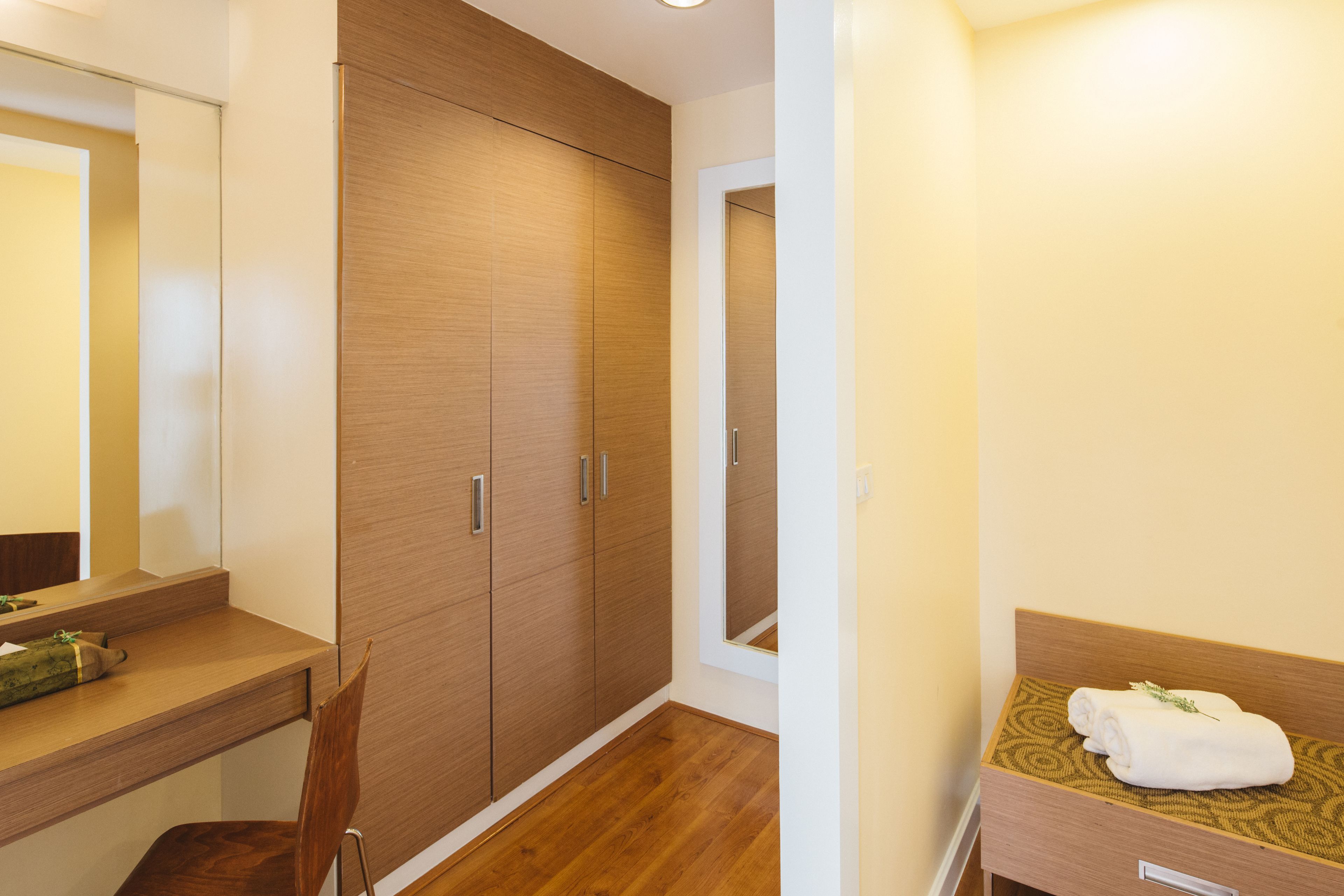 Een hotelkamer met een houten garderobe, een houten bureau, een stoel, een bed met een gestreept hoofdeinde en een spiegel.