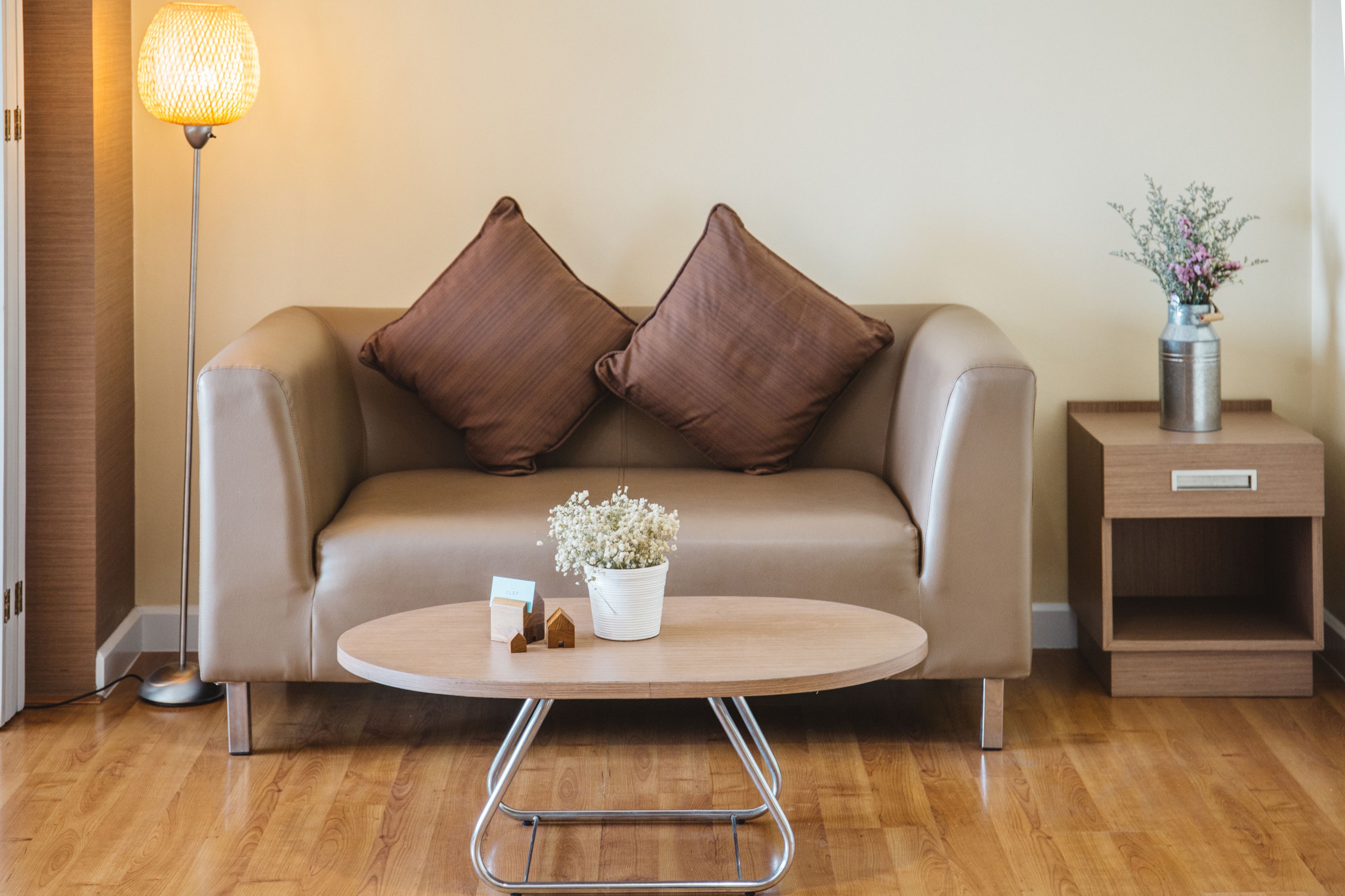 Ein modernes Wohnzimmer mit einer Couch, einem Couchtisch, einer Stehlampe, einem Beistelltisch mit einer Vase und einer kleinen Topfpflanze.