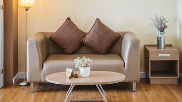 Ein modernes Wohnzimmer mit einer Couch, einem Couchtisch, einer Stehlampe, einem Beistelltisch mit einer Vase und einer kleinen Topfpflanze.