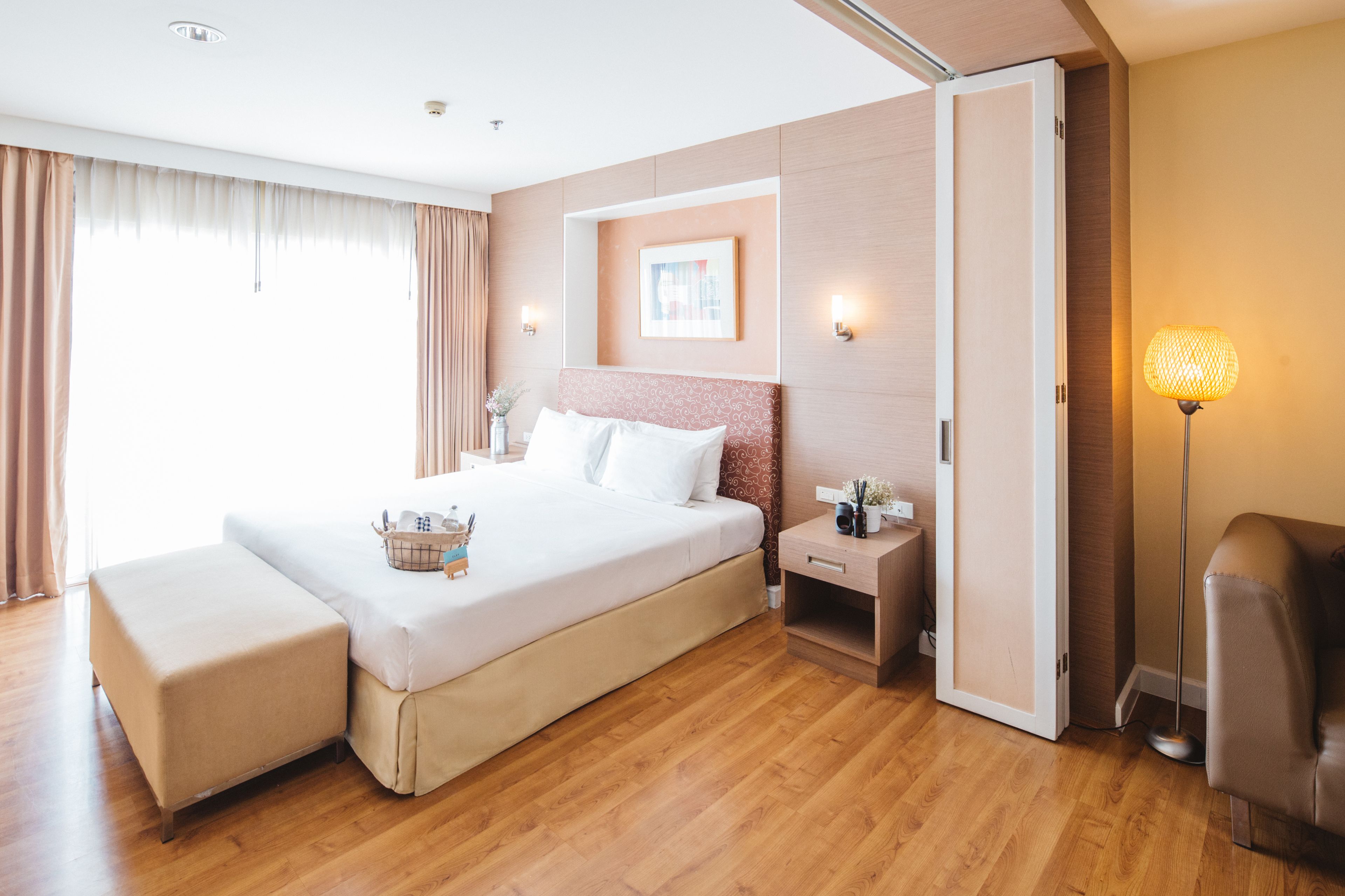 A modern hotel room with a large bed, bedside tables, a lamp, and a view of the outdoors.