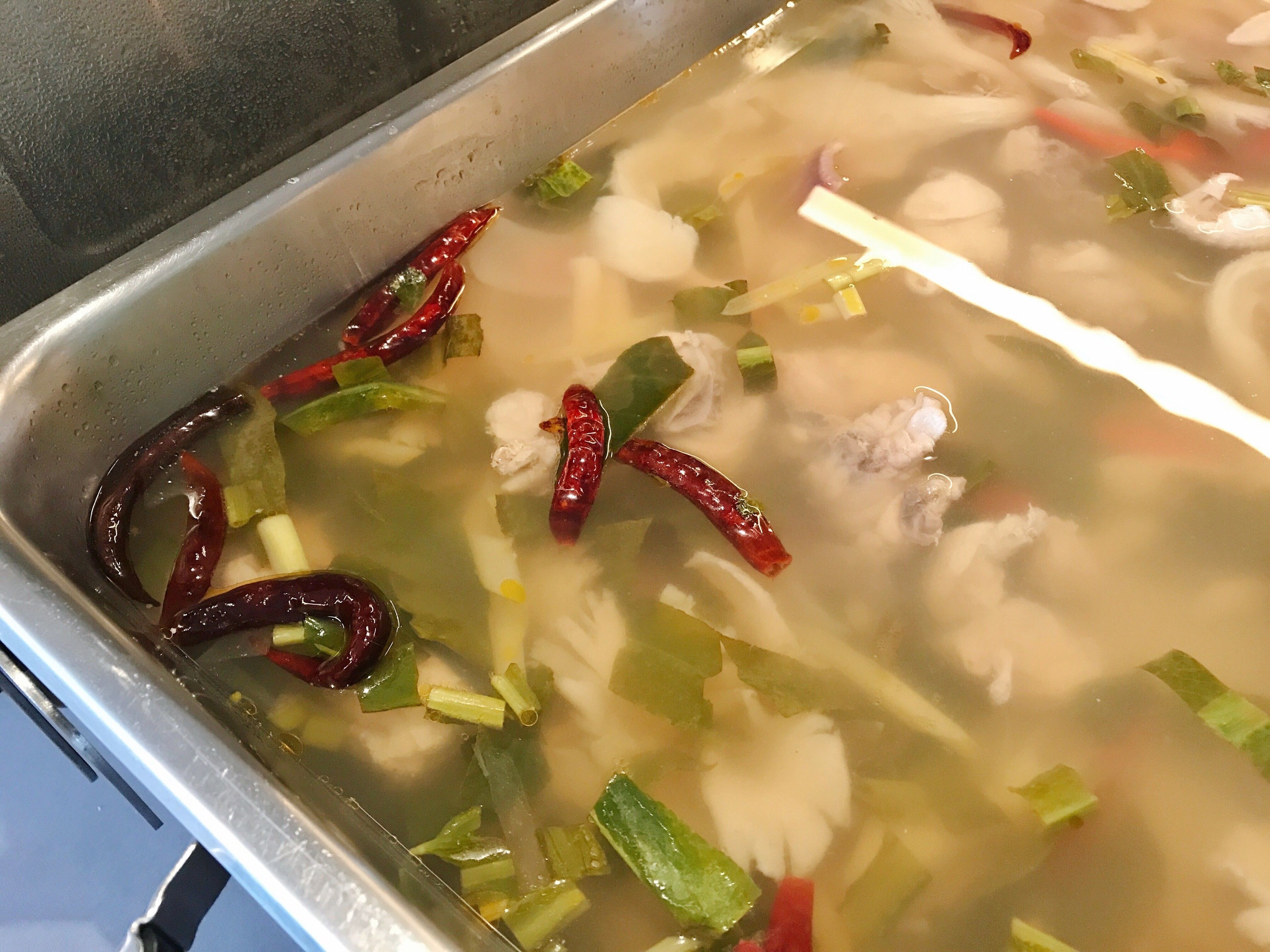 A stainless steel sink with a clear liquid containing vegetables and spices.