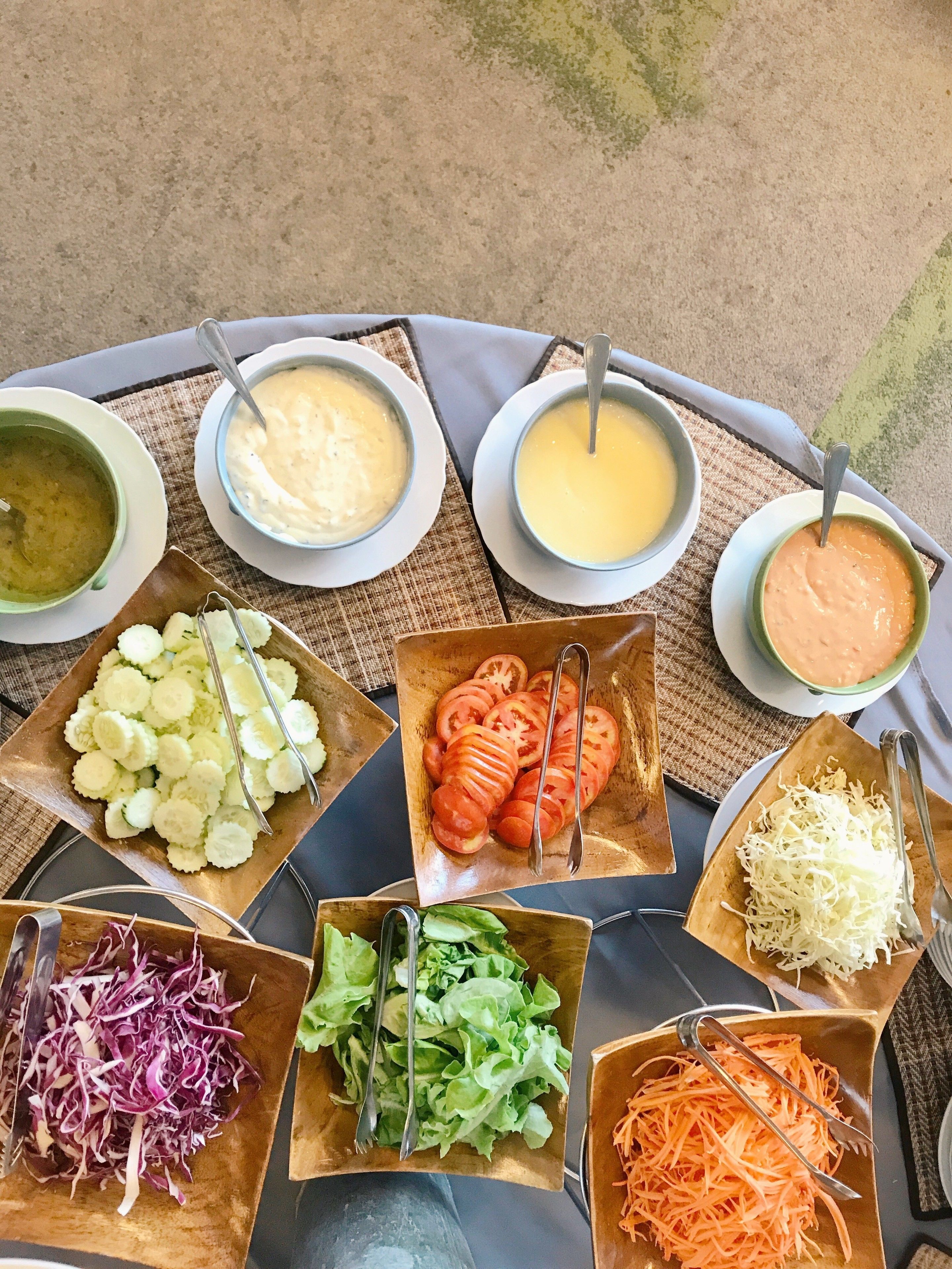A table with various food items and condiments, including bowls of soup, sliced vegetables, and shredded cheese.