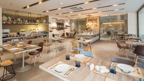 A modern restaurant with wooden tables and chairs, a visible menu board, and a kitchen area in the background. - Clef Hotel (Samut Prakan)