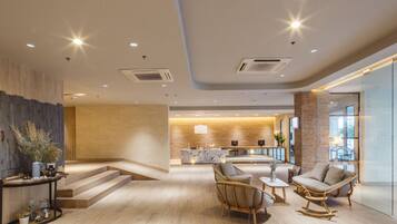 A modern lobby with a reception desk, seating area, and a staircase leading to upper floors.