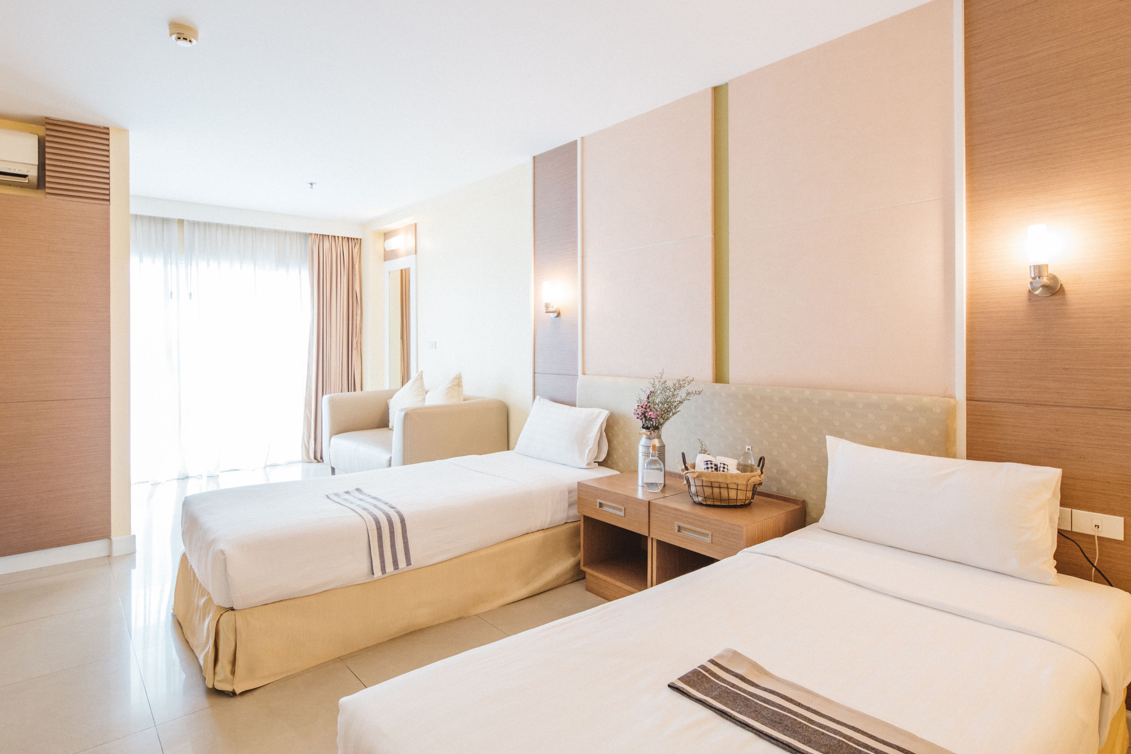 Ein Hotelzimmer mit zwei Betten, einem Nachttisch mit einer Vase und einem großen Fenster mit Vorhängen.