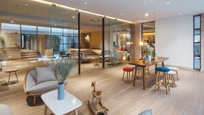A modern interior with a wooden floor, a seating area with a sofa and chairs, a dining table with stools, and a staircase leading to an upper level. - Clef Hotel (Samut Prakan)