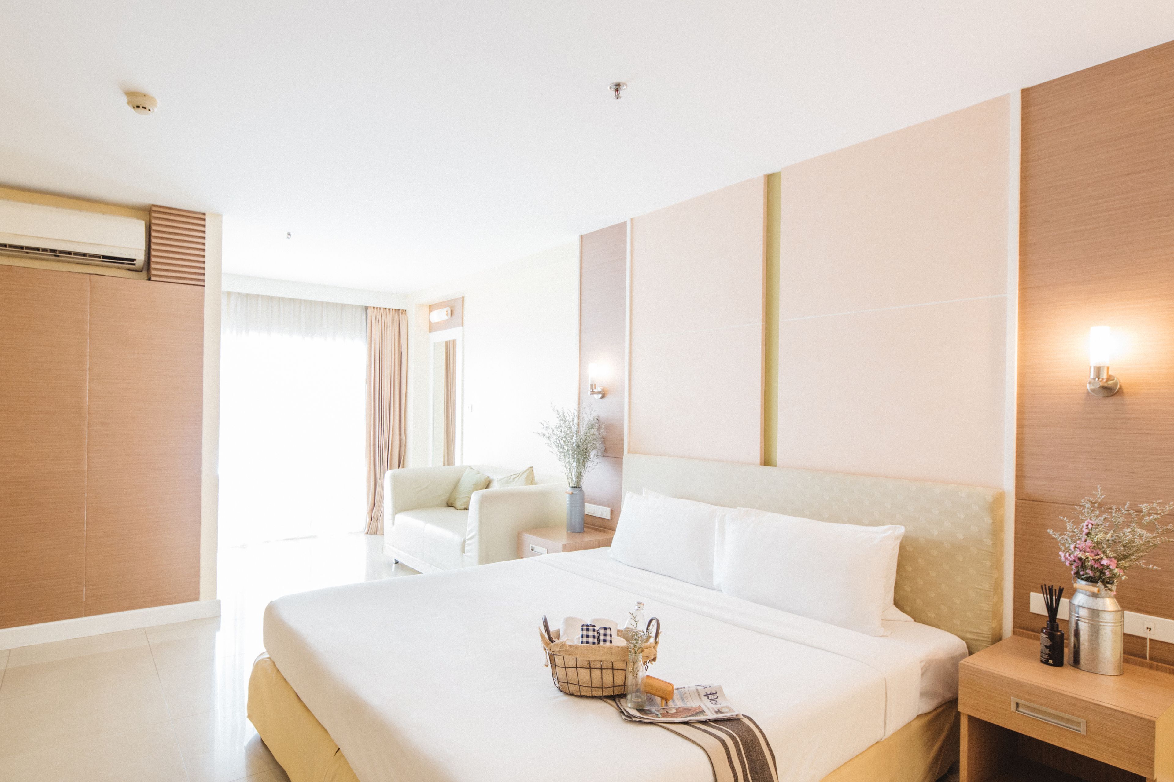 Habitación de hotel con una cama grande, una mesita de noche con lámpara, una pequeña mesa con un jarrón y una ventana con cortinas.