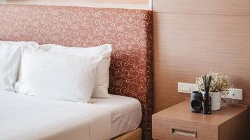 A neatly made bed with white linens, a patterned headboard, and a bedside table with a vase of flowers and a black object.