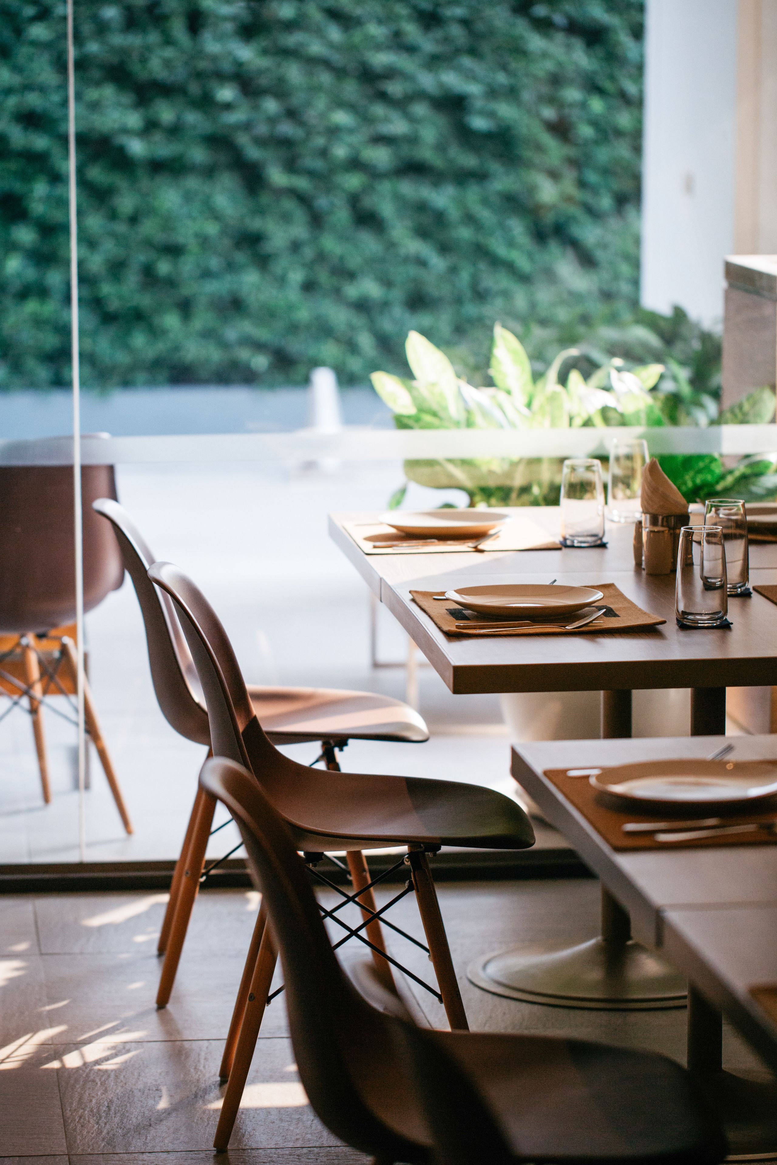 Un coin repas avec une table dressée pour deux personnes, des chaises et une vue sur la verdure environnante.