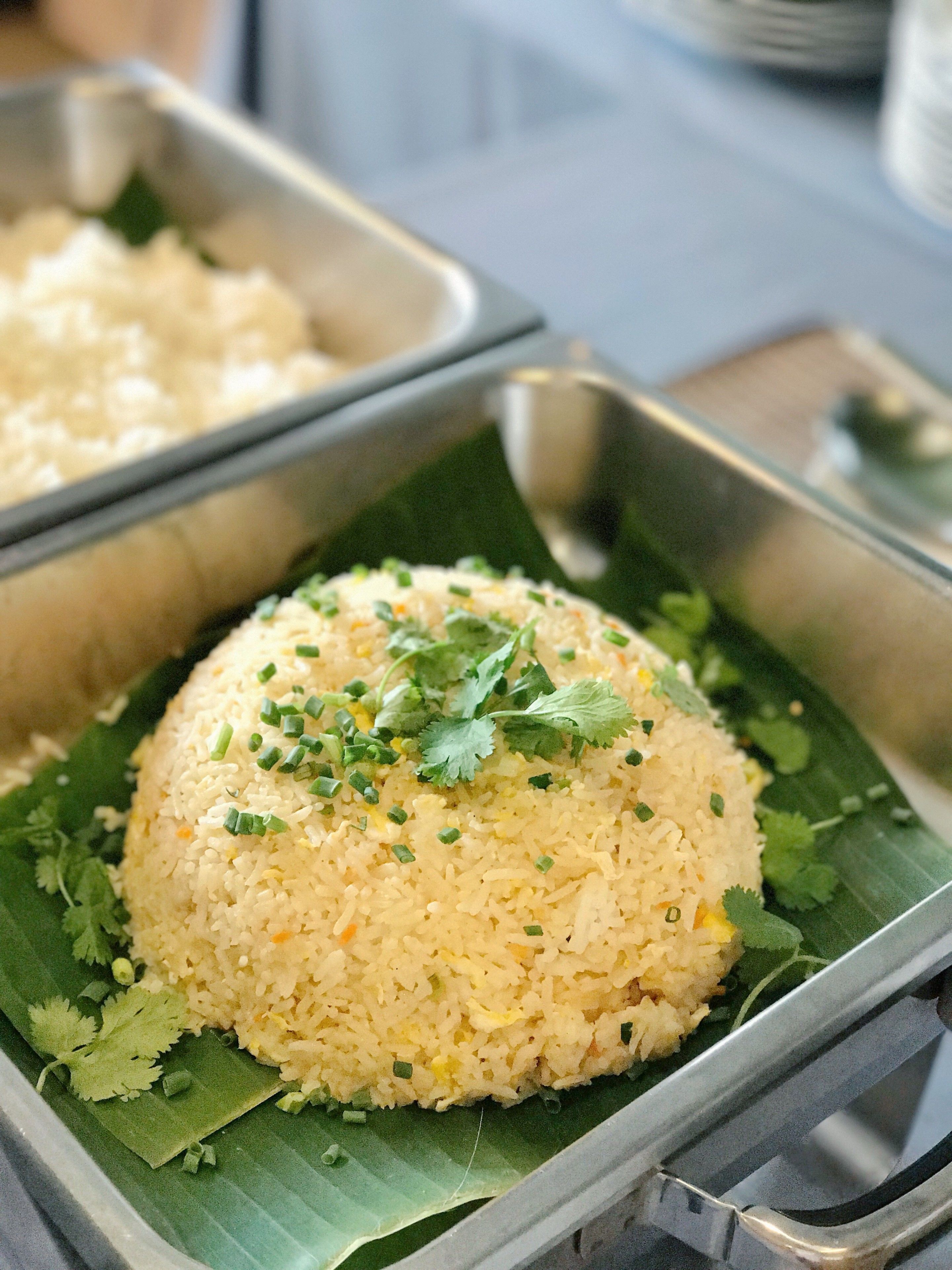 A tray of fried rice garnished with green onions and cilantro, served on a banana leaf.