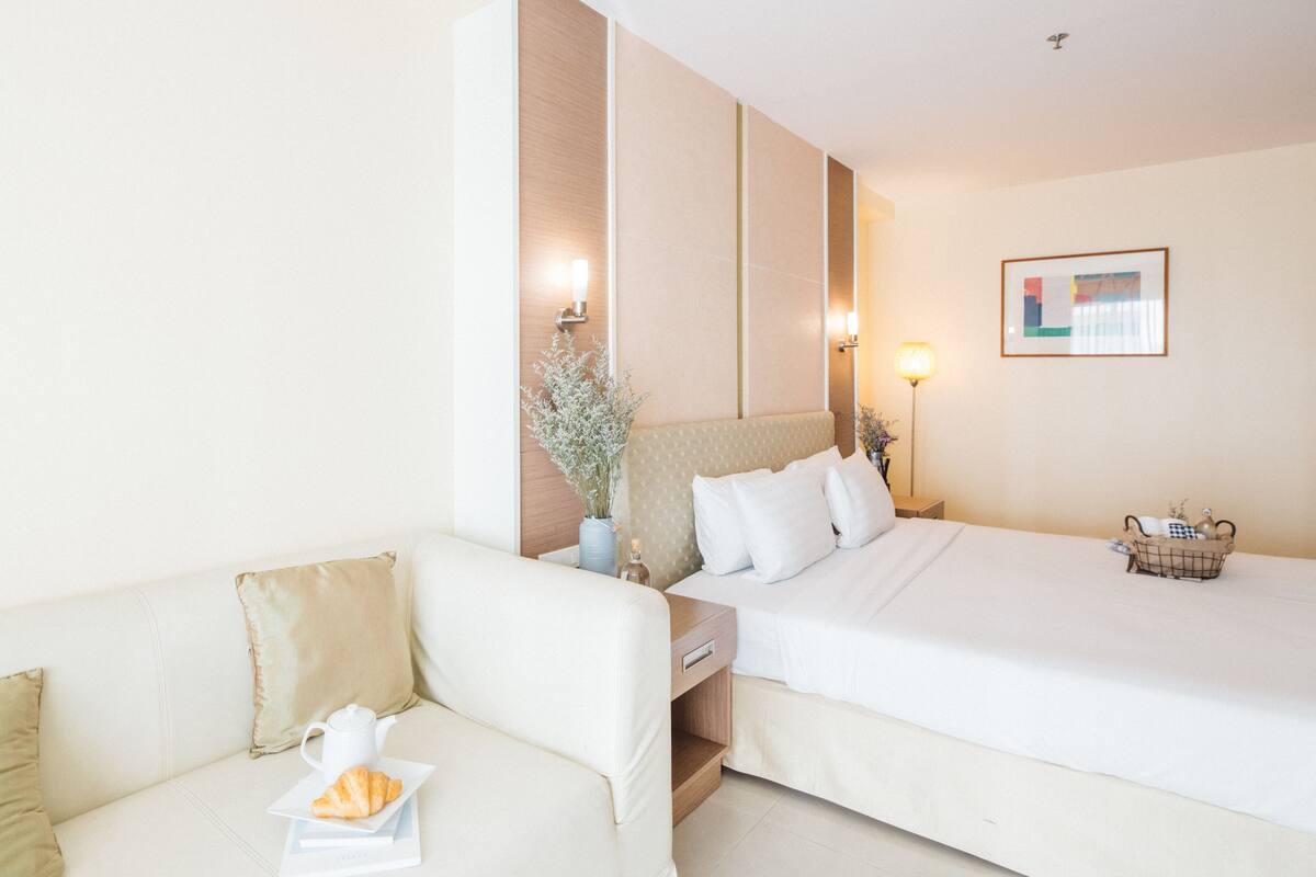 Una habitación de hotel con una cama, un sofá, una mesita de noche con una lámpara y un cuadro en la pared.
