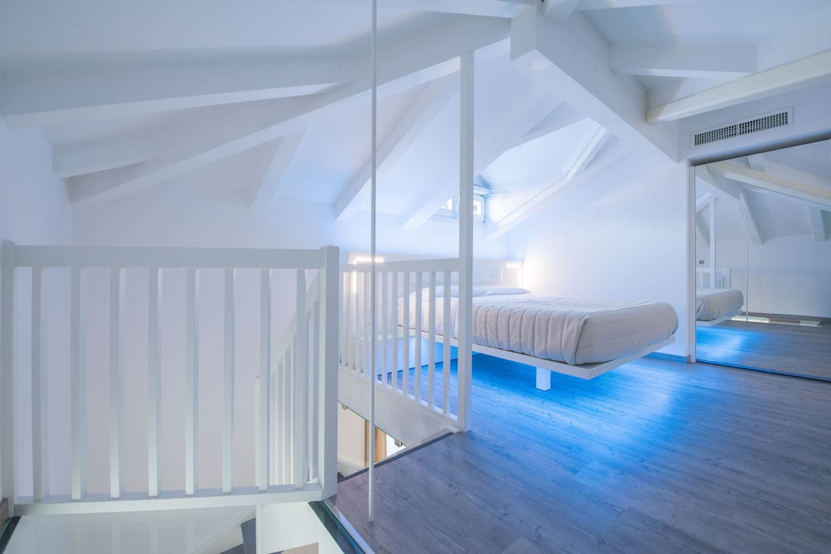 A modern loft bedroom with a sloped ceiling, a bed, and a staircase.