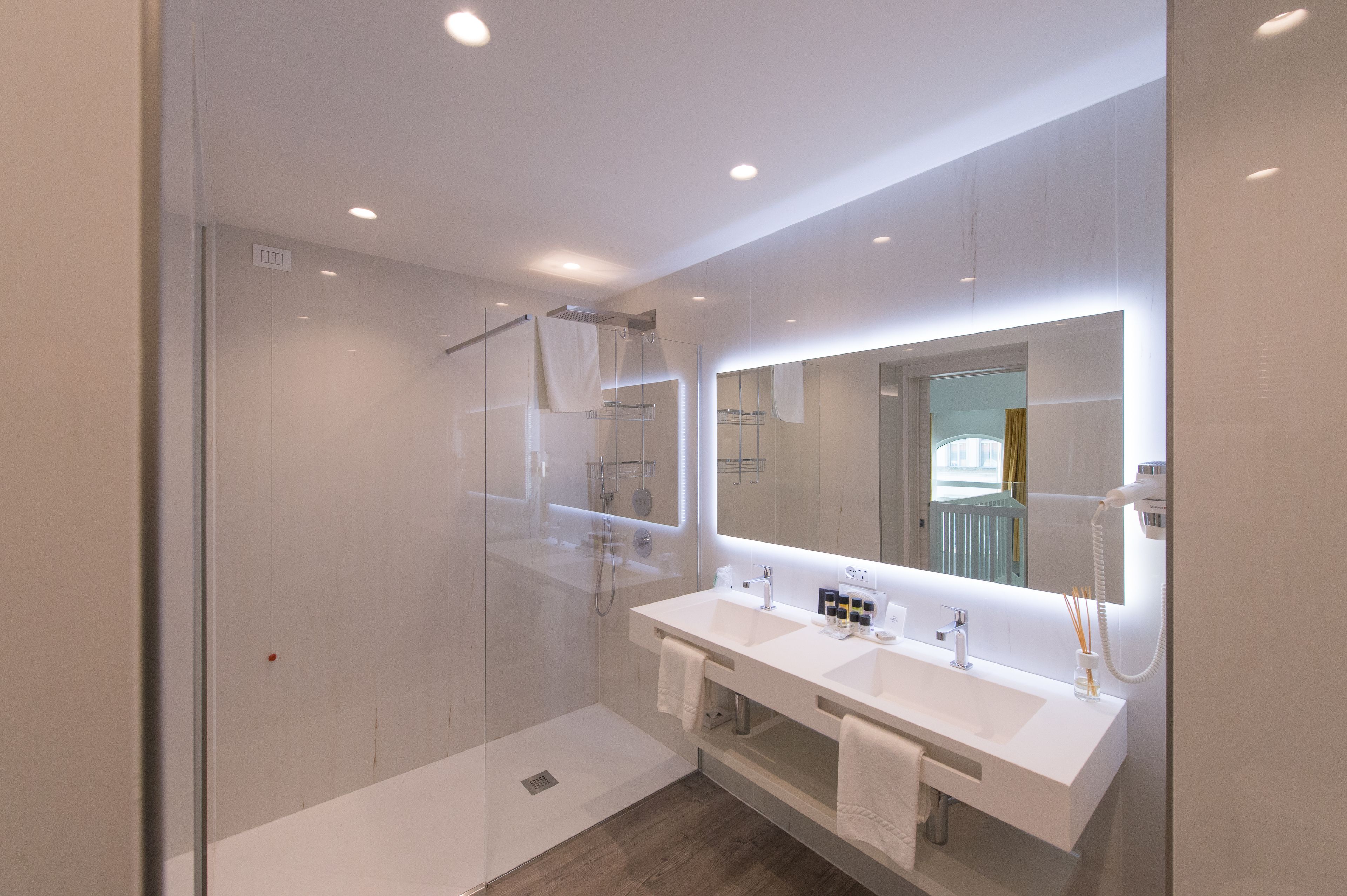 Une salle de bain moderne avec une douche à l’italienne en verre, un meuble-lavabo à deux vasques et un grand miroir.