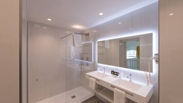 Une salle de bain moderne avec une douche à l’italienne en verre, un meuble-lavabo à deux vasques et un grand miroir.