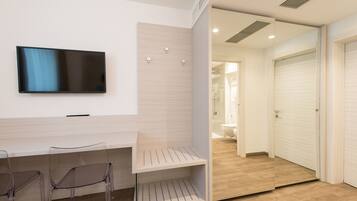 A modern hotel room with a flat-screen TV mounted on the wall, a wooden desk, and a seating area with chairs.