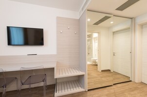 Quarto de hotel moderno com televisão de tela plana na parede, escrivaninha de madeira e área de estar com cadeiras.
