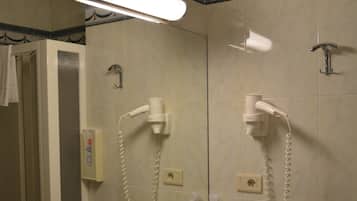 Un baño con lavamanos, espejo y dos secadores de pelo fijados a la pared.