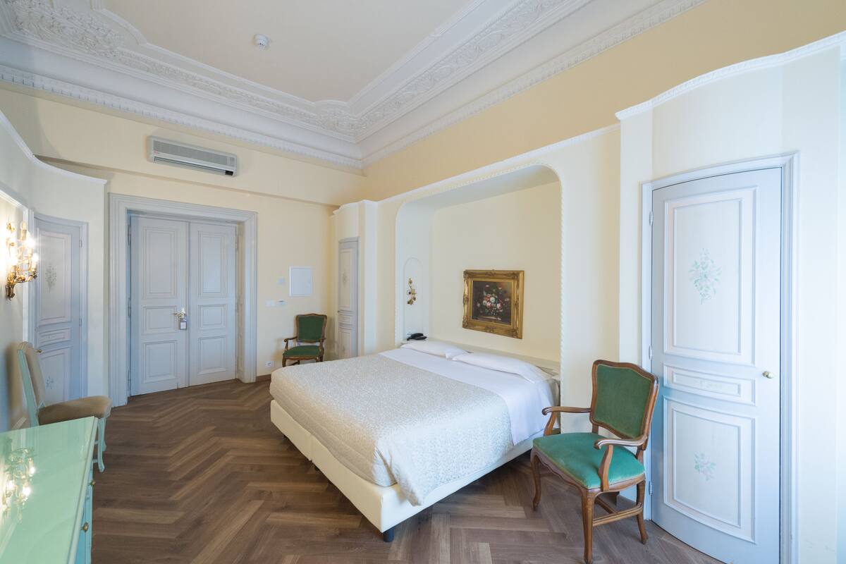 A hotel room with a large bed, two chairs, a dresser, and a door with decorative paneling.