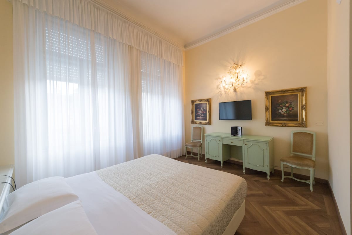 A hotel room with a large bed, a desk with two chairs, a television, and two framed pictures on the wall.