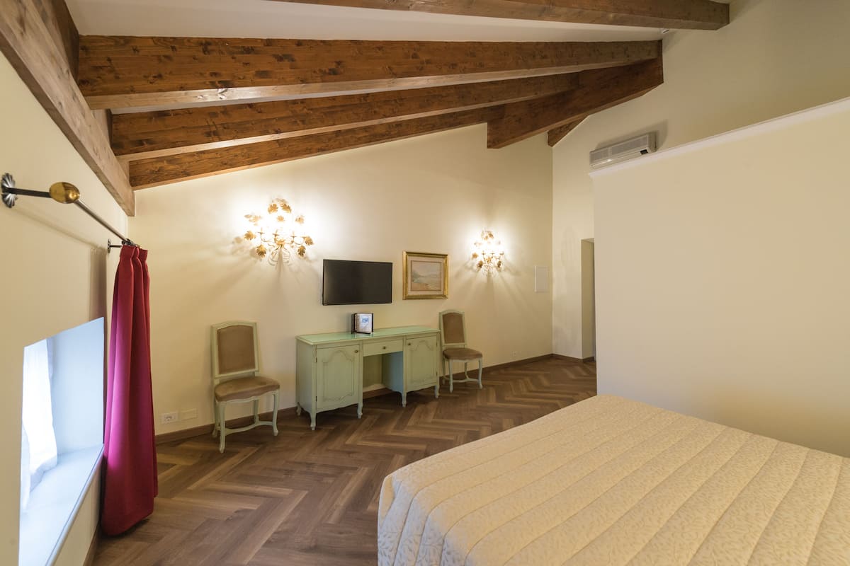 A bedroom with a wooden ceiling, a bed, a desk with two chairs, a television, and wall sconces.
