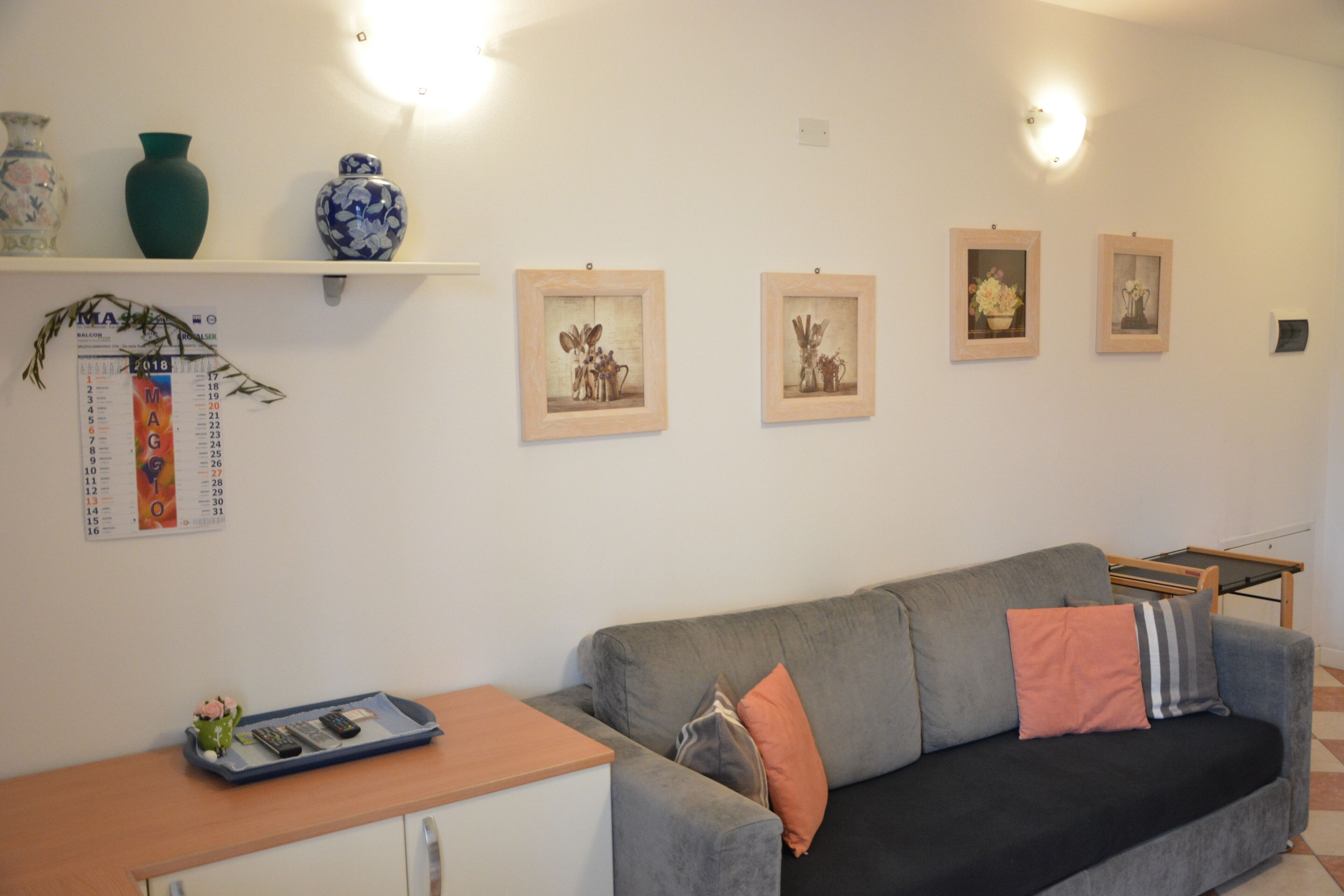 A living room with a grey sofa, a wooden side table, and a small shelf with decorative items.
