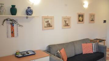 A living room with a grey sofa, a wooden side table, and a small shelf with decorative items.