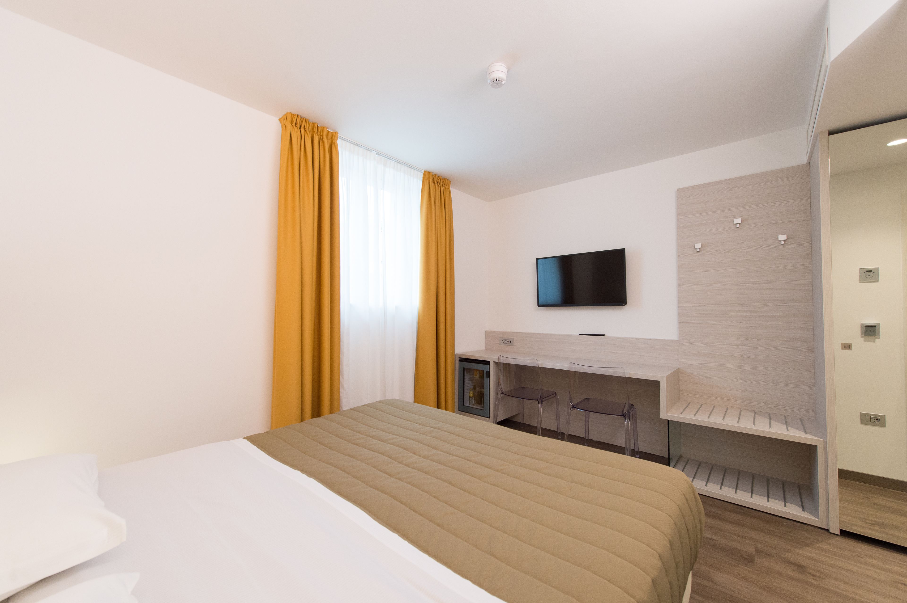 A modern hotel room with a bed, a desk, and a TV.