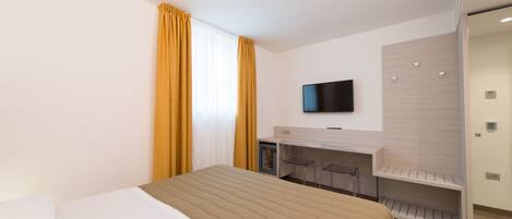 A modern hotel room with a bed, a desk, and a TV.