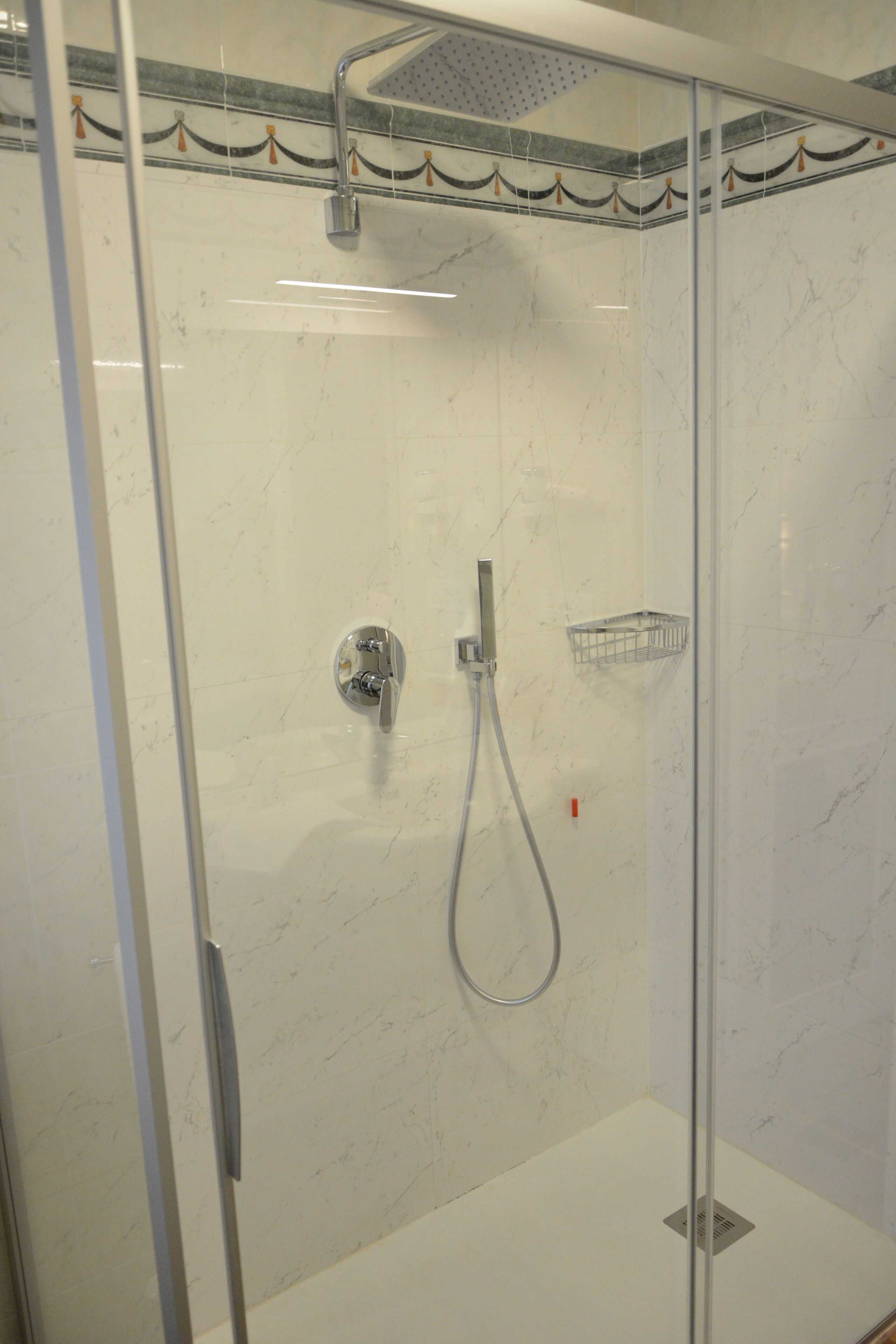A glass-enclosed shower with a handheld showerhead and a wall-mounted faucet.