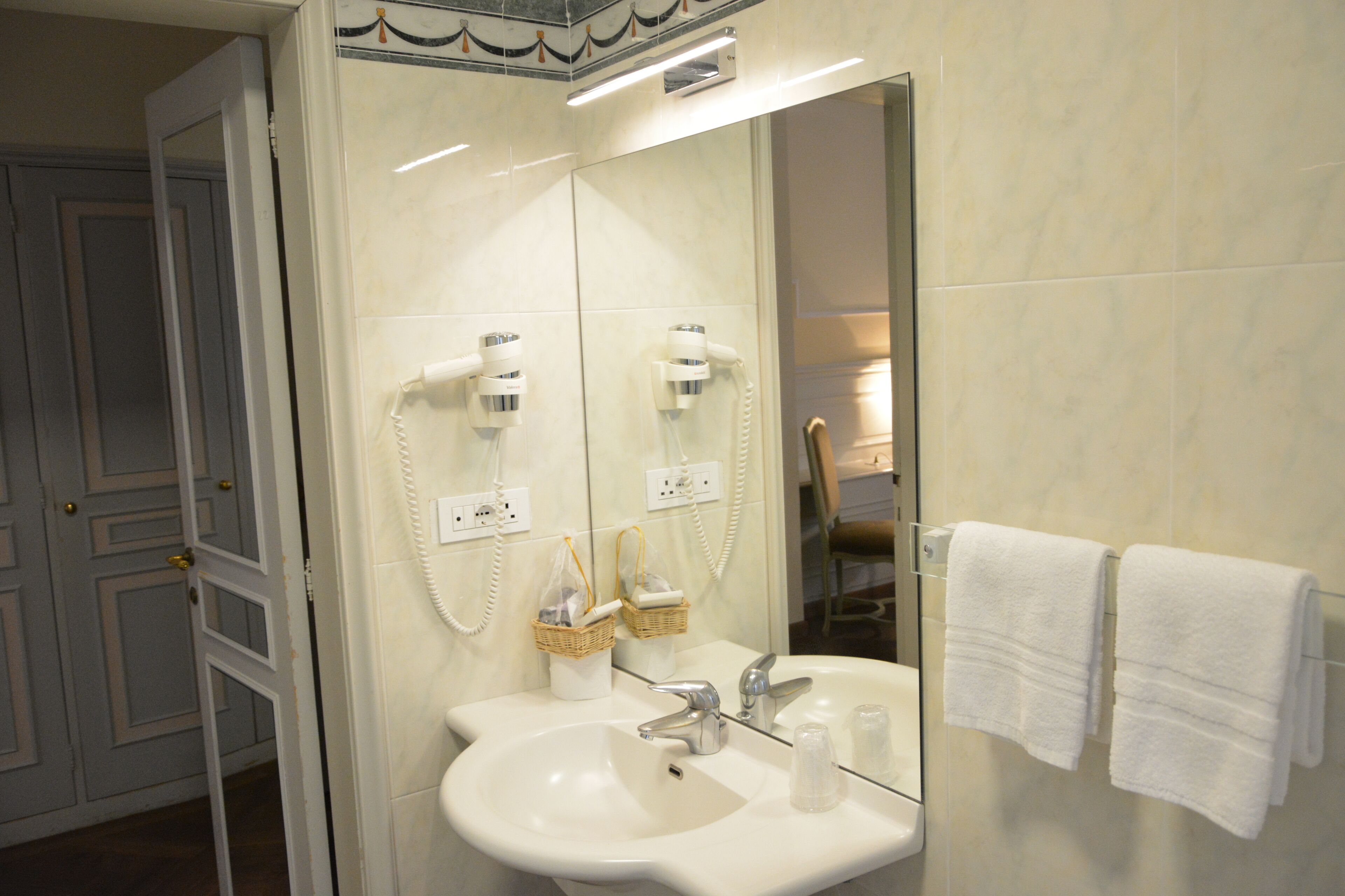 A bathroom with a sink, two hair dryers, a mirror, and towels on a rack.