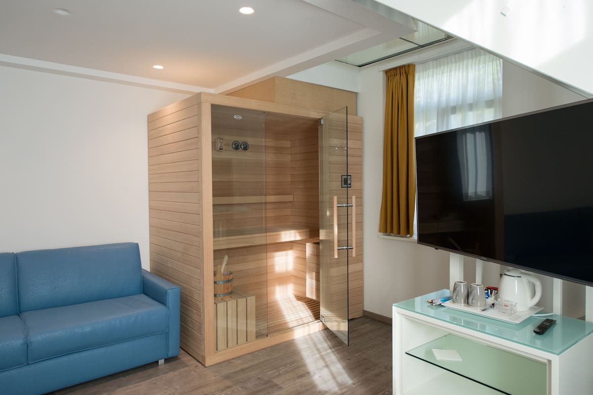 A modern hotel room with a glass shower enclosure, a flat-screen TV, a glass coffee table, and a blue sofa.
