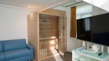 Ein modernes Hotelzimmer mit Duschkabine aus Glas, einem Flachbildfernseher, einem Glastisch und einem blauen Sofa.