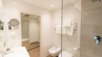 A modern bathroom with a glass shower enclosure, a bidet, and a vanity with a mirror and hairdryer.