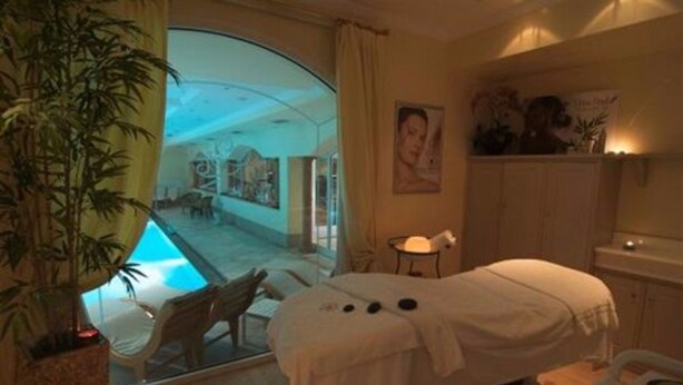 Un cuarto de spa con una camilla de masaje, una mesita con una lámpara y vista a un área de piscina exterior.