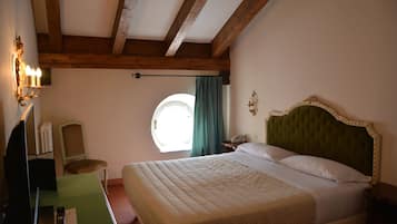 A bedroom with a large bed, a desk with a chair, a lamp, and a window with curtains.