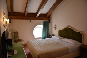 A bedroom with a large bed, a desk with a chair, a lamp, and a window with curtains.