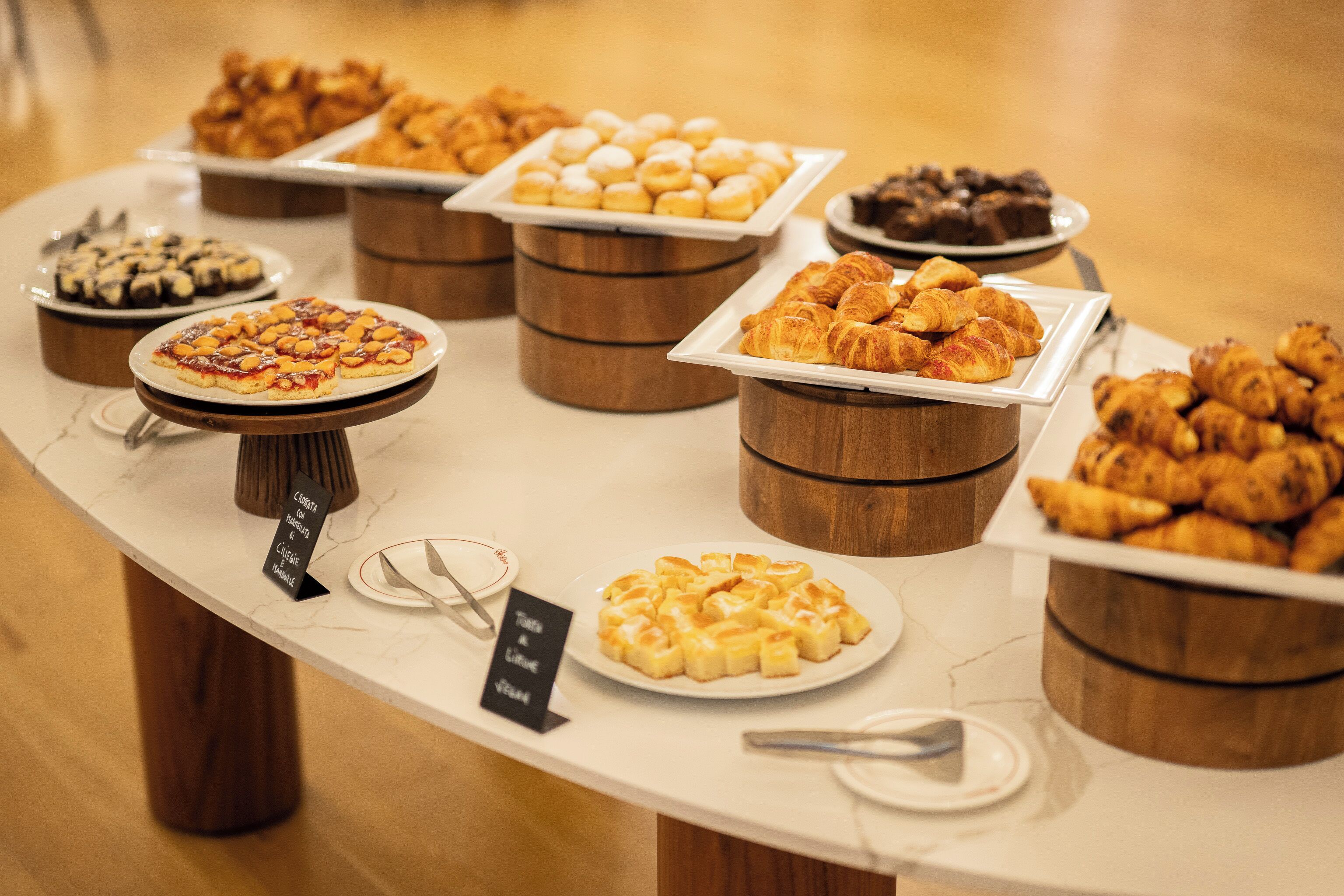A buffet with various pastries and desserts displayed on wooden stands and plates.