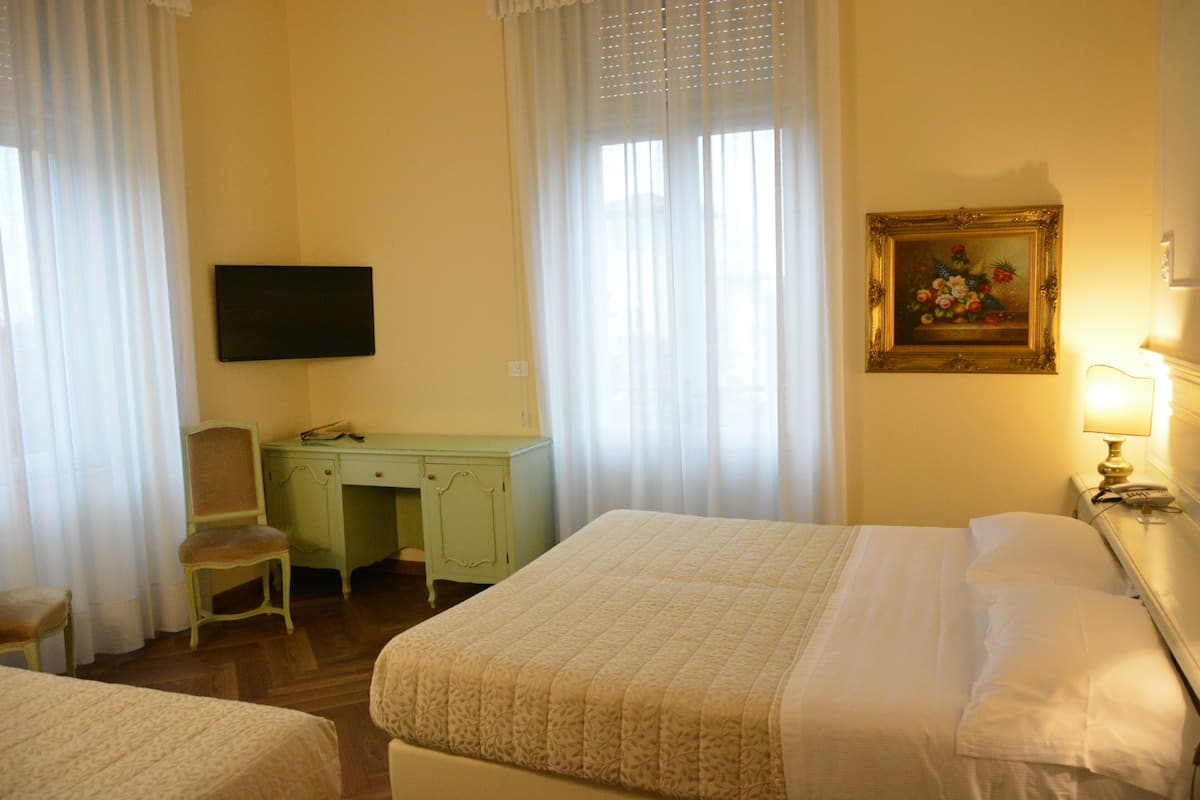 A hotel room with a bed, a desk, a chair, a television, and a painting on the wall.