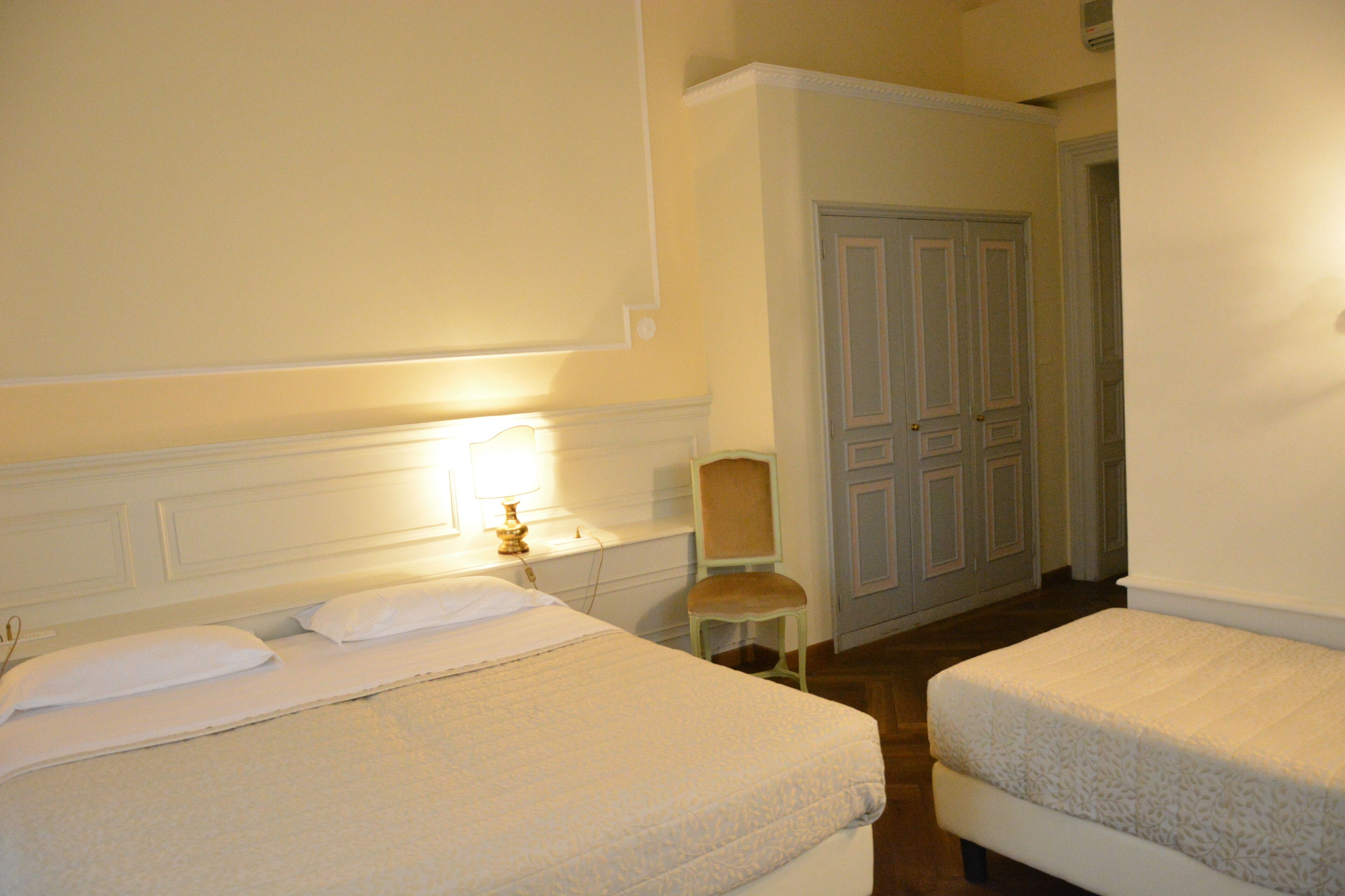 A hotel room with two beds, a chair, and a door leading to another room.