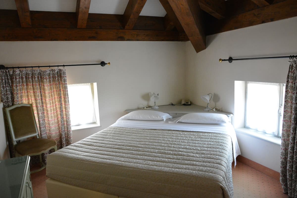 A bedroom with a large bed, two bedside tables, a chair, and a window.