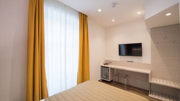 Ein modernes Hotelzimmer mit einem Bett, einem Schreibtisch mit Stuhl, einem Fernseher und einem Kleiderschrank.